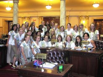 Girls Scouts in uniforms gathered around desk.